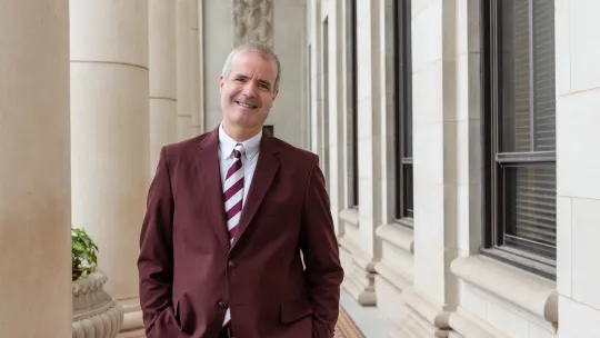 Provost Alan Sams standing outside white building in maroon suit