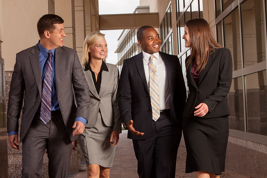 Four students all dressed in suits walk while smiling and talking business.